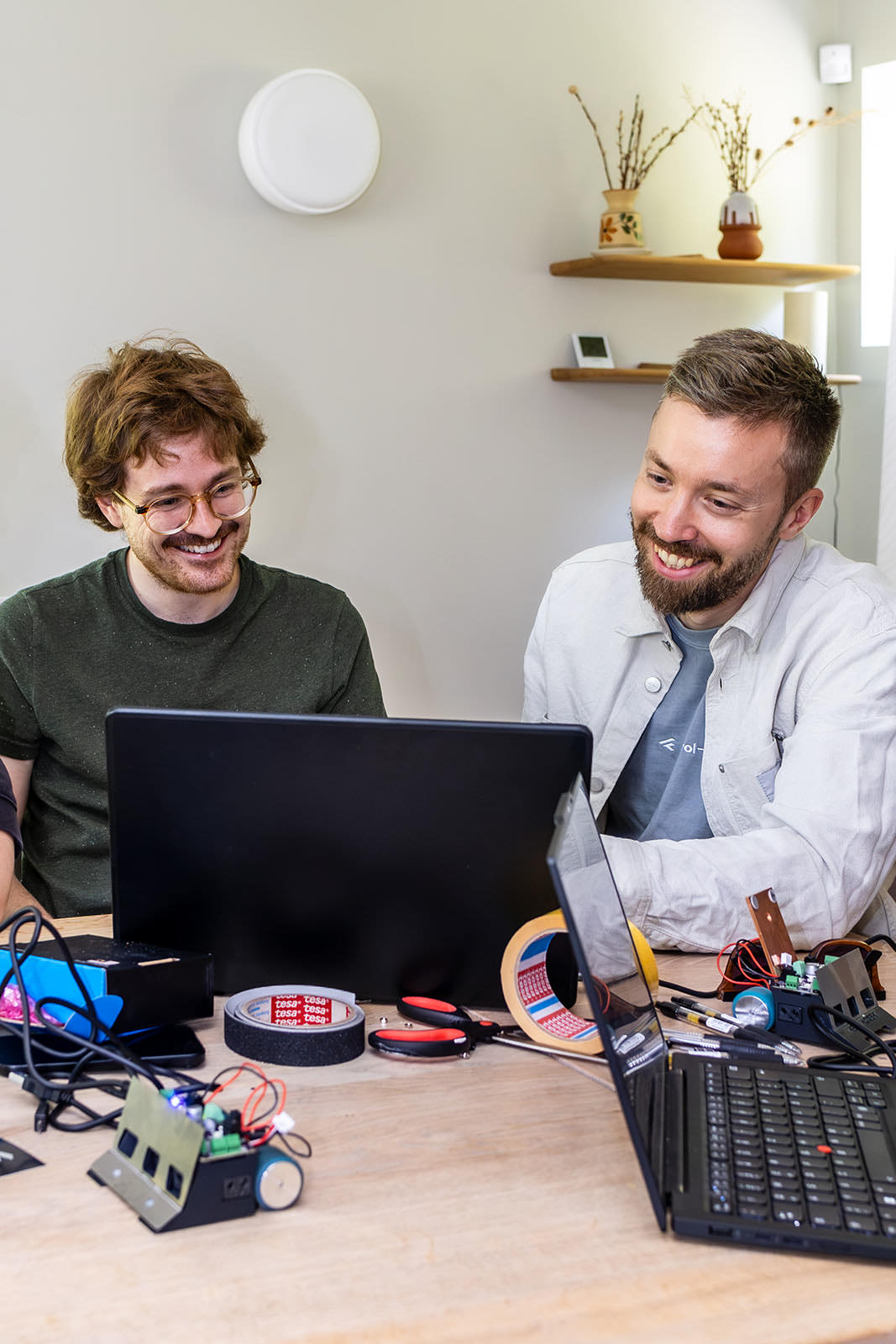 Zwei Kollegen am Laptop, davor eine aufgebaute Sensorplatine mit Kabeln und Werkzeug