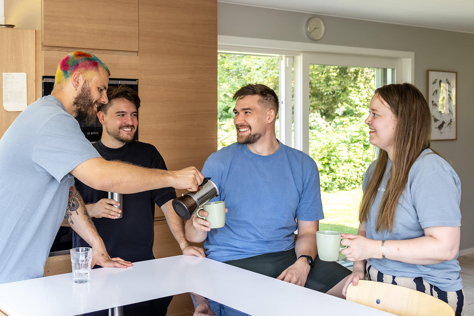 Vier Personen in der Büroküche, einer schenkt Kaffee aus einer Kanne ein