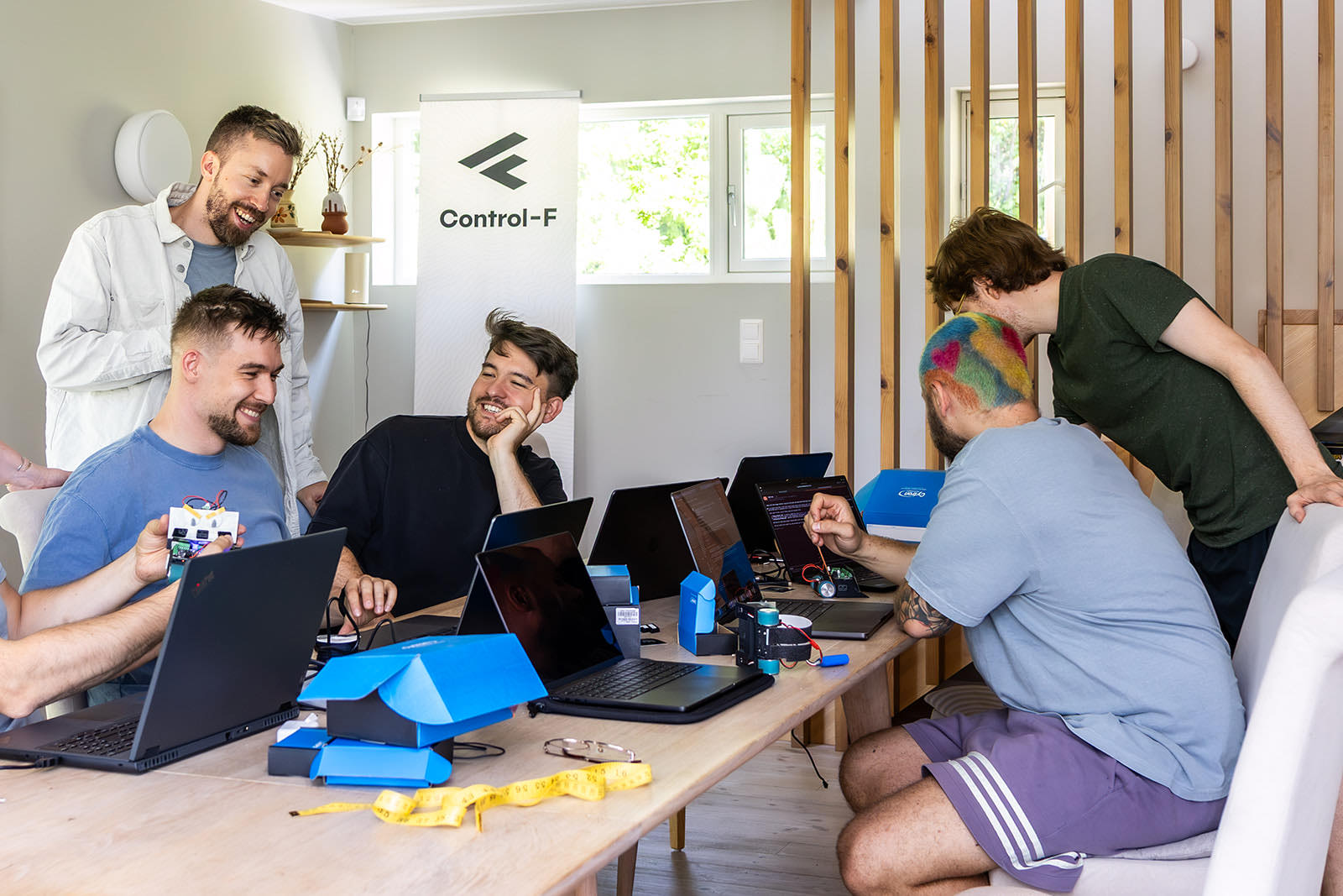 Das Team an einem langen Tisch im Büro, Laptops und Messtechnik zwischen den Plätzen